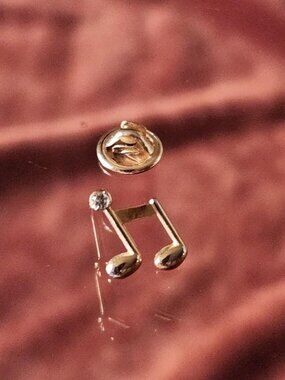 Small gold-tone music note lapel pin with single rhinestone accent.